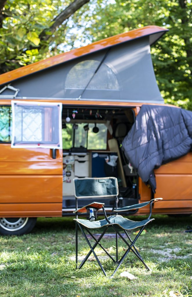 Camper in campsite. Outdoor equipment and travel van on green me